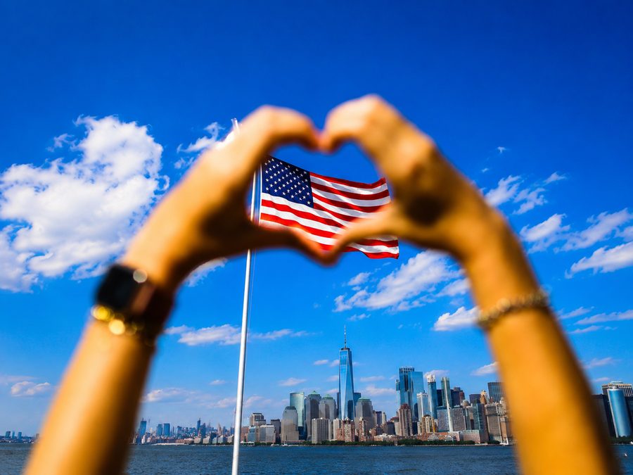 Hands forming a heart around the American flag, New York skyline behind
